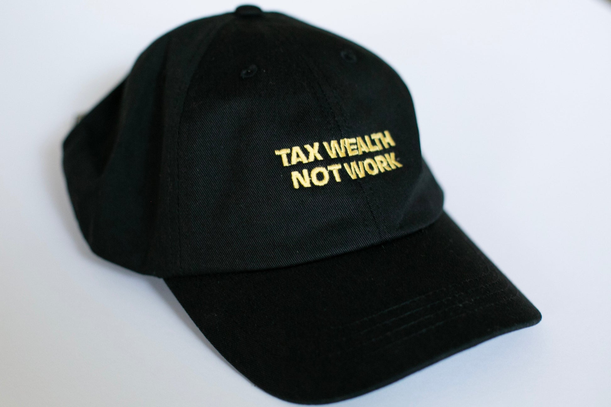 Black cap with 'TAX WEALTH NOT WORK' text in gold on a white background